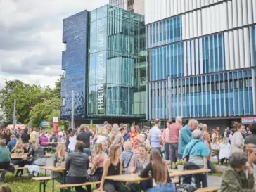 Menschengruppen sitzen Draußen vor der Rhein-Mosel-Halle